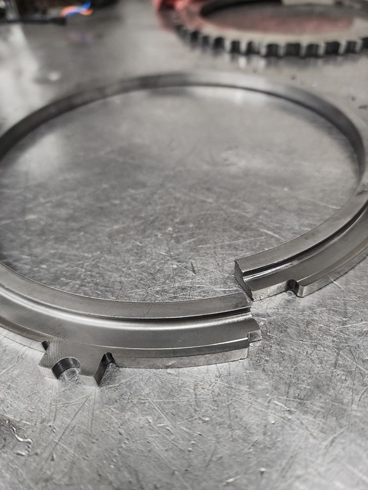 Close-up of a segmented metal ring with a gap and notched edges, resting on a metallic surface.