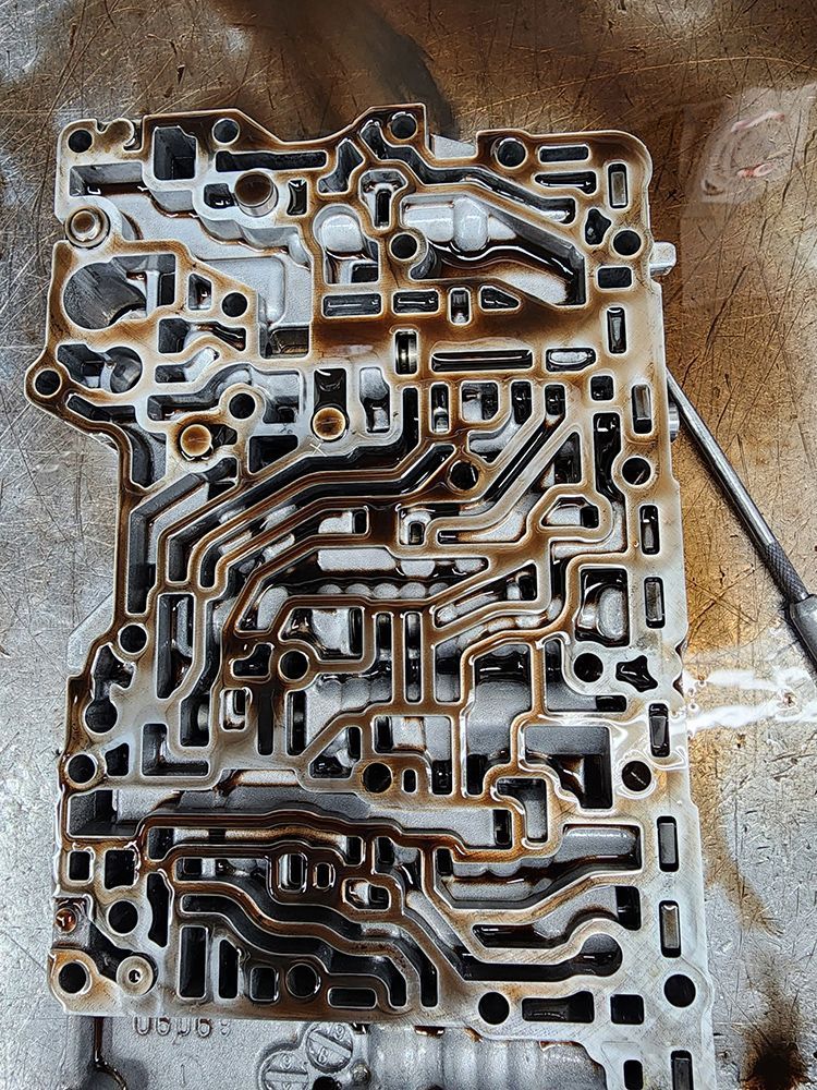Transmission valve body with fluid residue, showing channels and pathways.