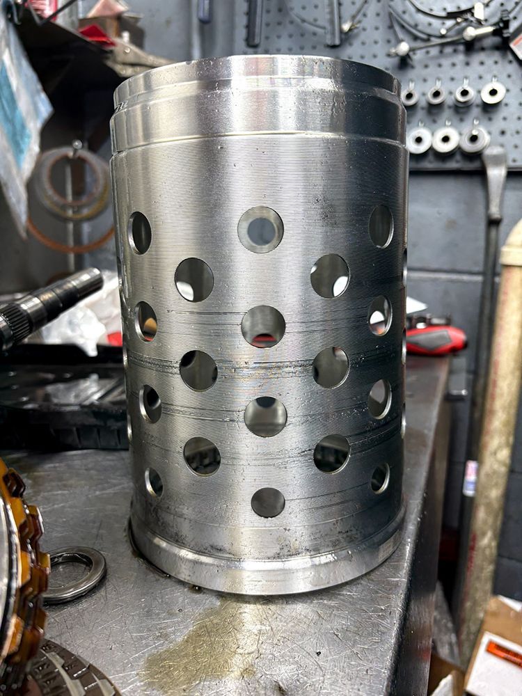Cylindrical metal part with numerous round holes, possibly automotive, on a workbench.