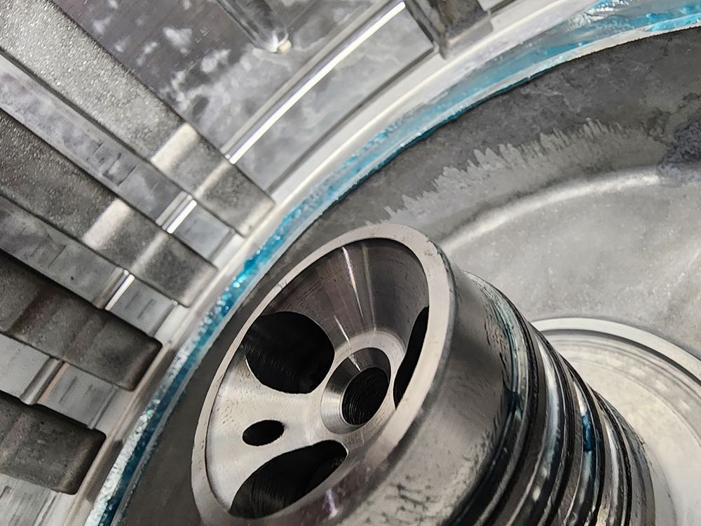 Close-up of a machine component, showing a silver metal circular piece with multiple openings, and surrounding metal structures.