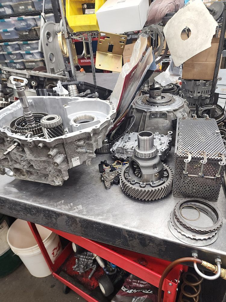 Disassembled car transmission parts on a workbench in a mechanic's shop.