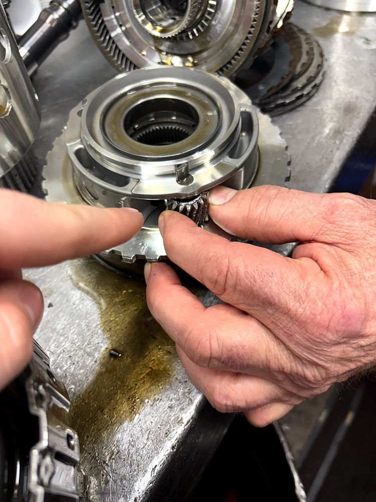 Hands assembling gears within a transmission component on a work surface.