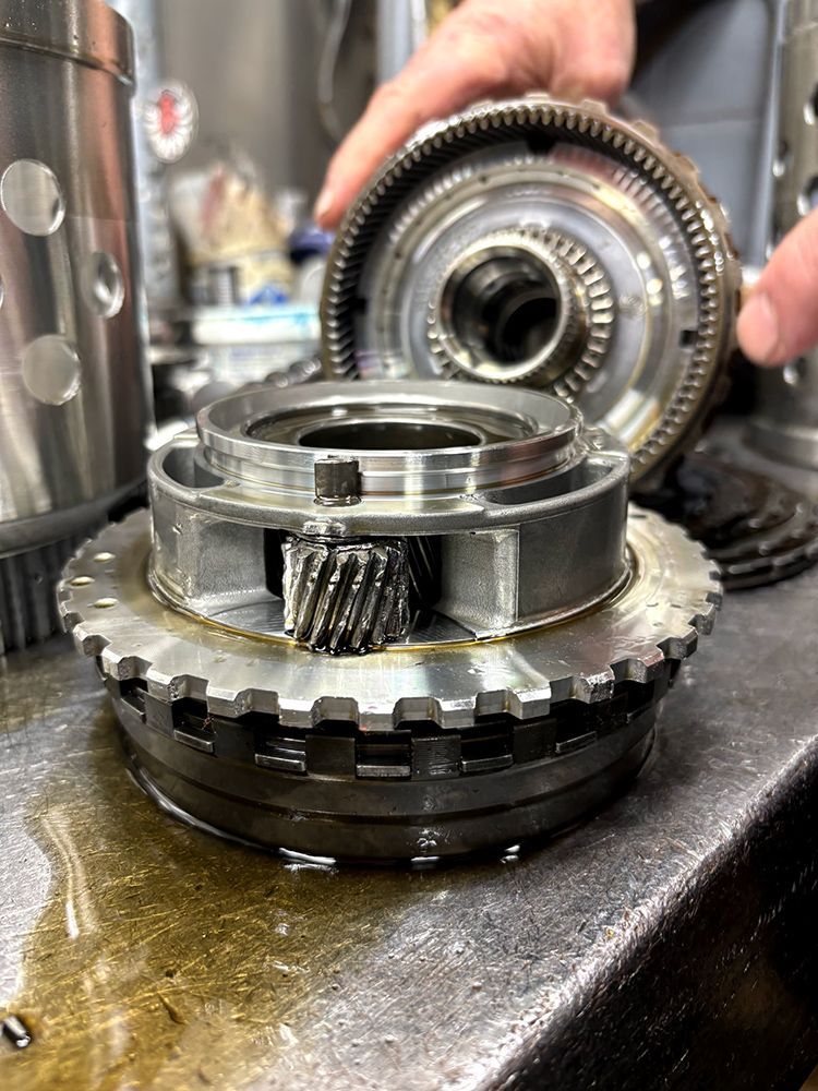 Disassembled transmission components on a workbench: gear, drum, and other metal parts.