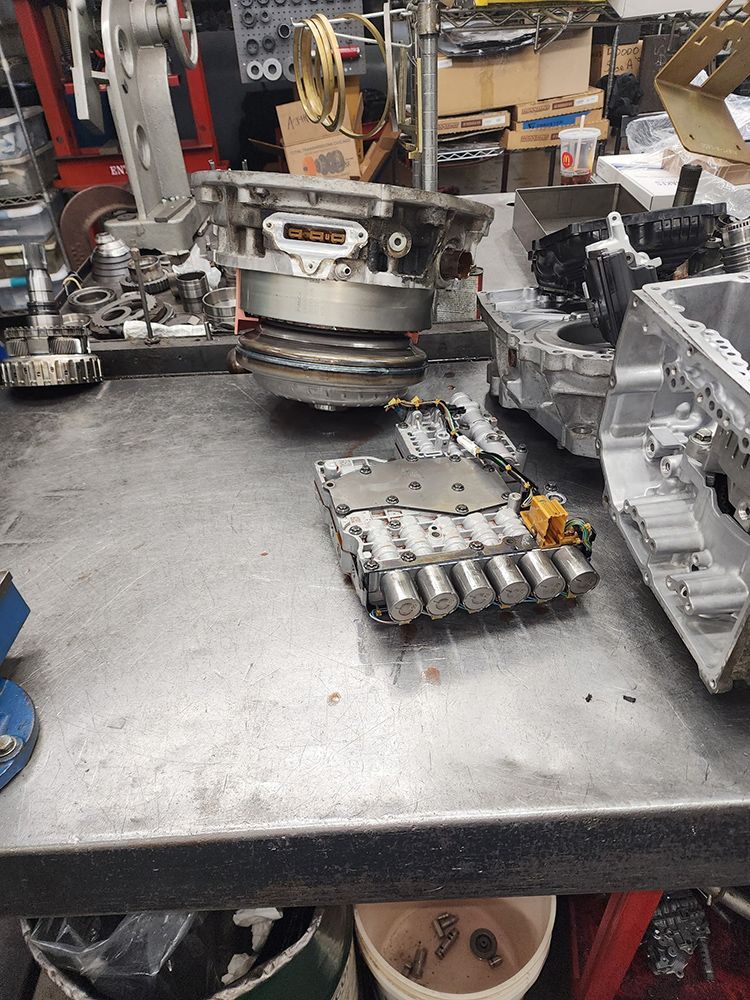 Disassembled car transmission parts on a metal workbench in a repair shop.