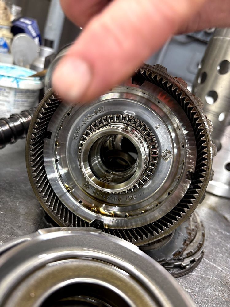 Close-up of a disassembled automatic transmission component with multiple gears, finger pointing towards the center.