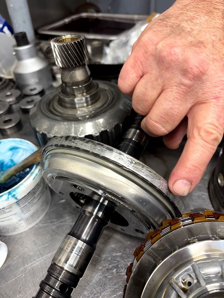Person's hand assembling transmission parts. Gears, shafts, and grease on a table.