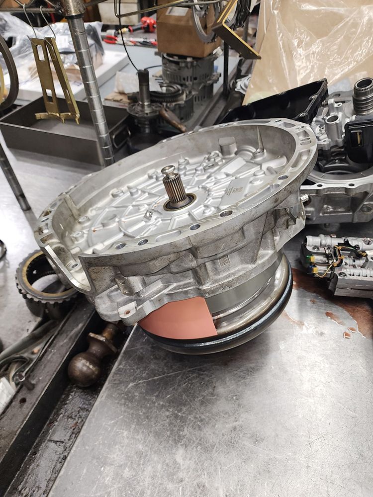 A disassembled car transmission on a metal table, showing gears and housing.