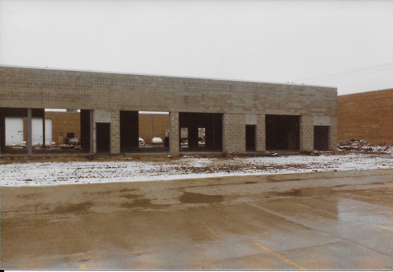 Building under construction with open entryways, visible concrete blocks, and some snow on the ground.