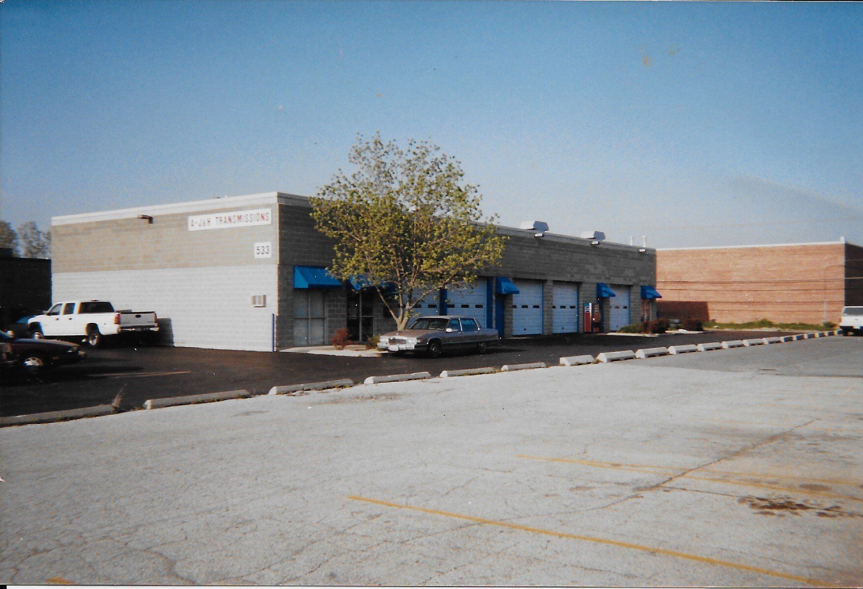 A commercial building with three garage doors and parked cars on a sunny day.