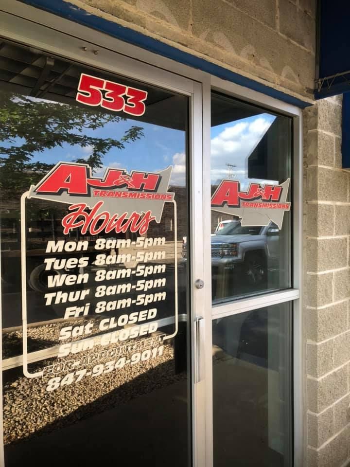 Sign for A & J Flooring with hours and phone number on a glass door. Building exterior with a brick wall.