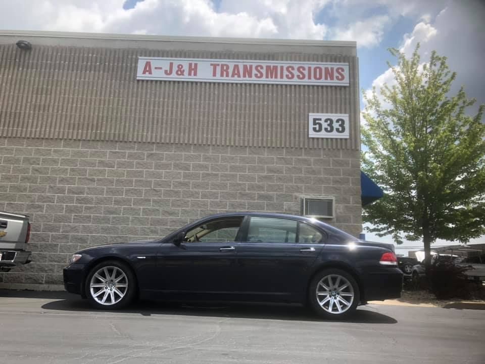 Dark sedan parked outside A-J&H Transmissions building with address 533. Blue sky.