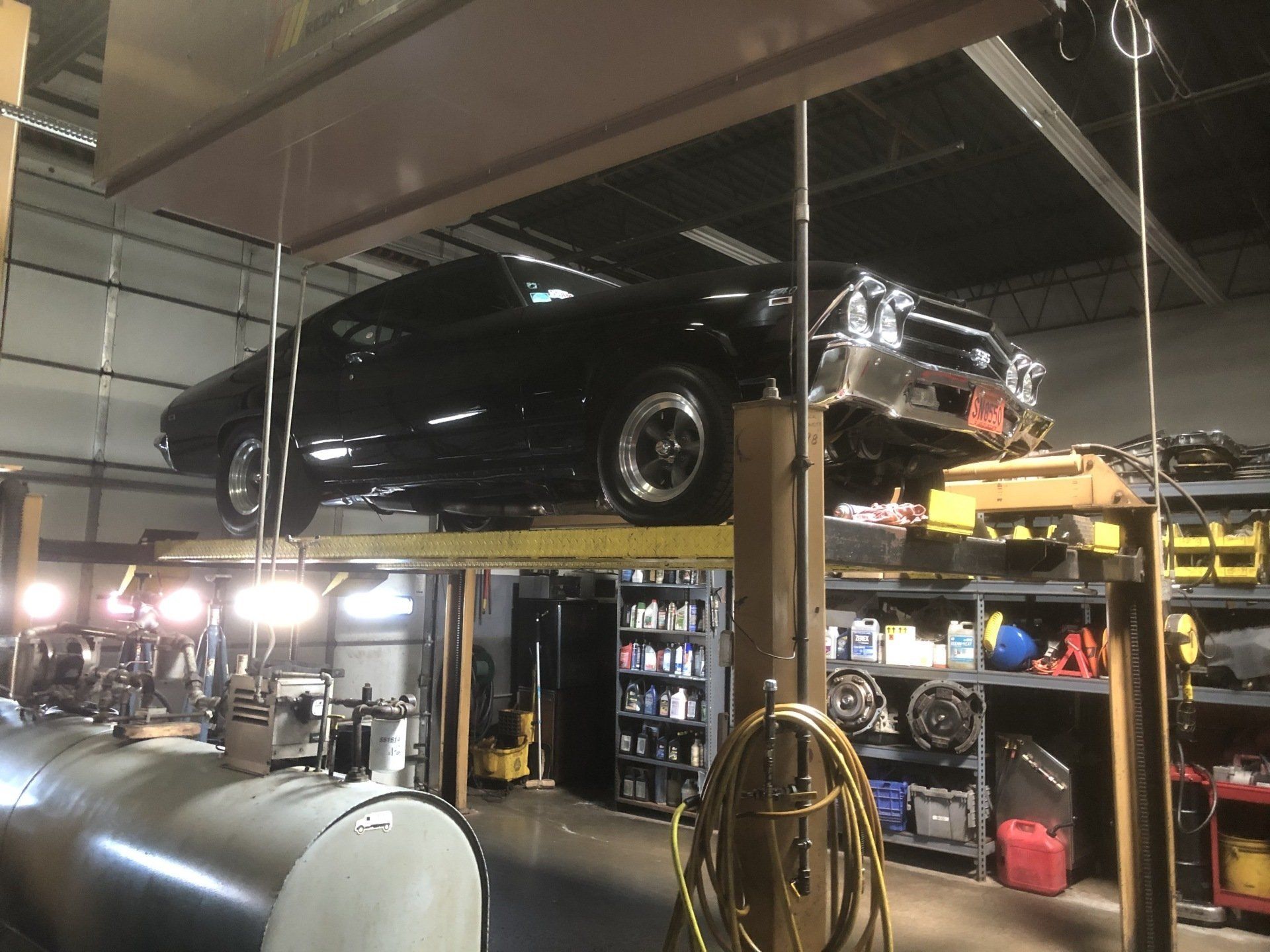 Black car on a lift in a garage with tools and equipment.