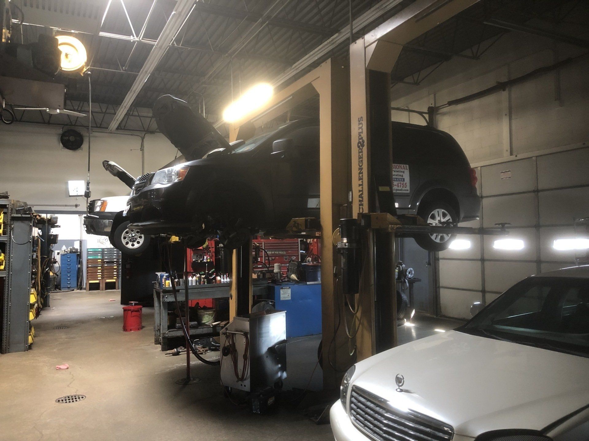 Cars on lifts inside an auto repair shop. One has its hood open. Tools and equipment are present.
