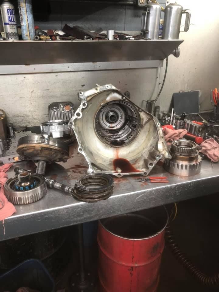 Disassembled car transmission on a workbench, with visible components and reddish fluid.