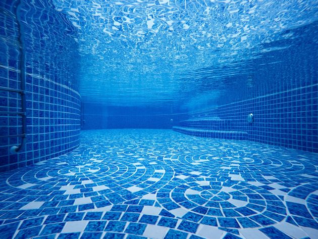 Empty blue-tiled swimming pool underwater, with rippling light across the floor and walls