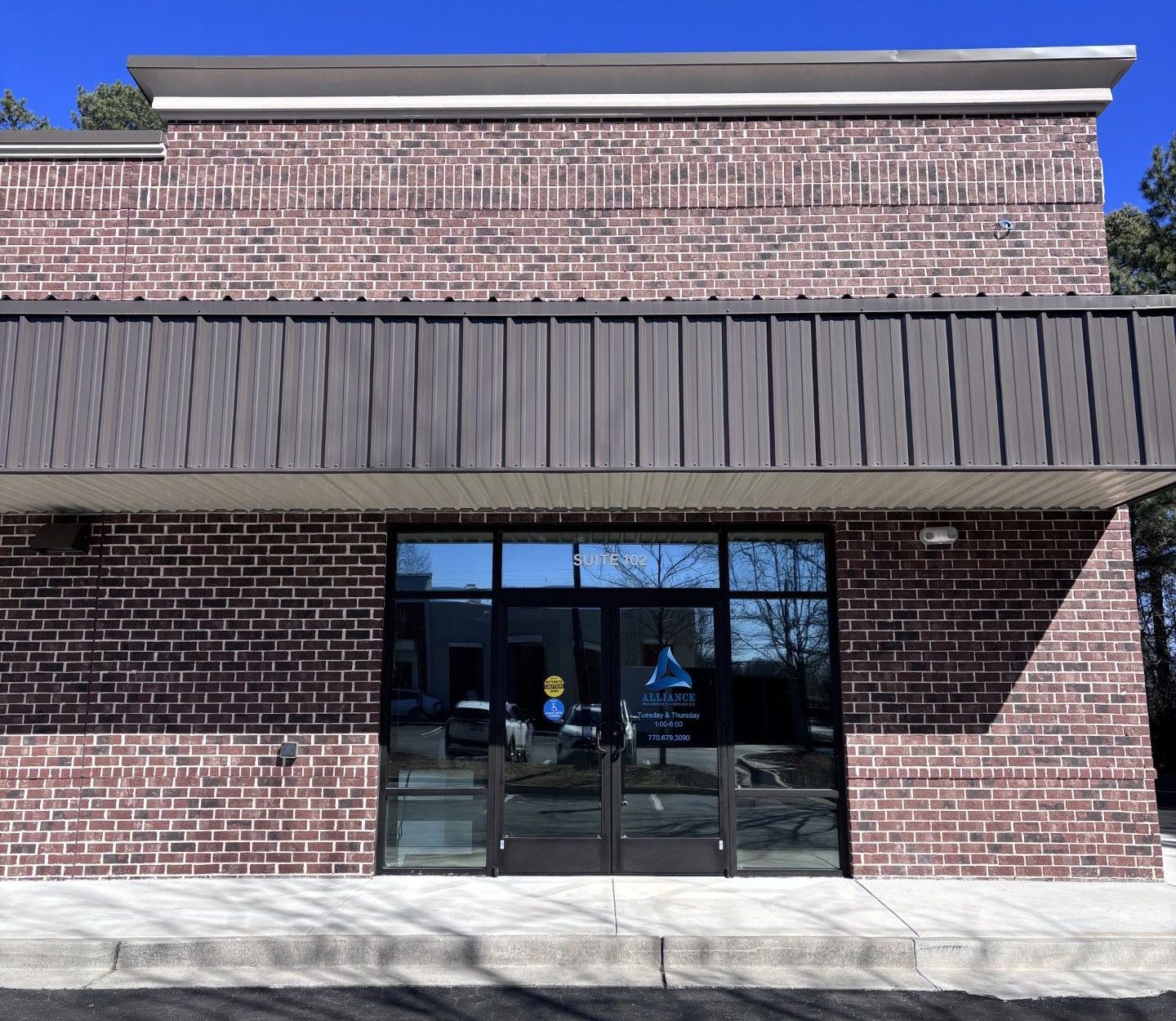 Brick building with glass doors and a dark awning under a clear blue sky.