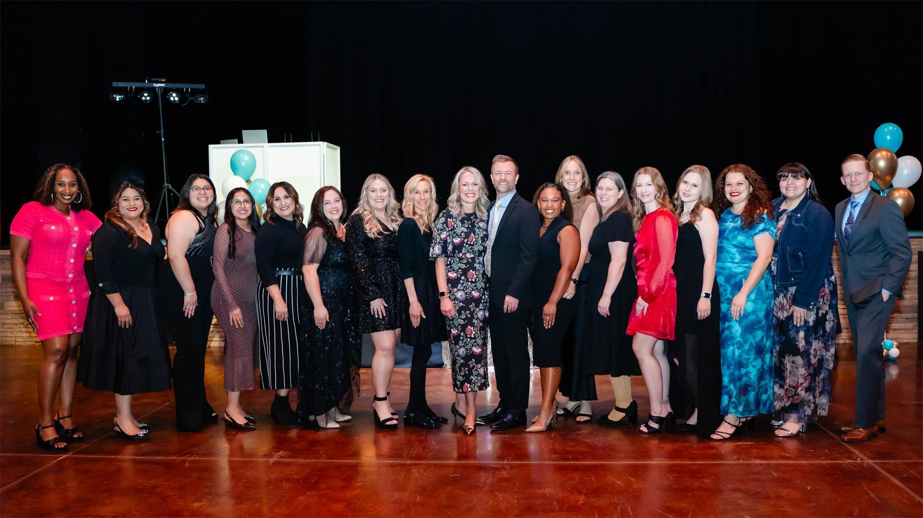 A group of people dressed in formal attire stand in a line on a stage during a formal event.