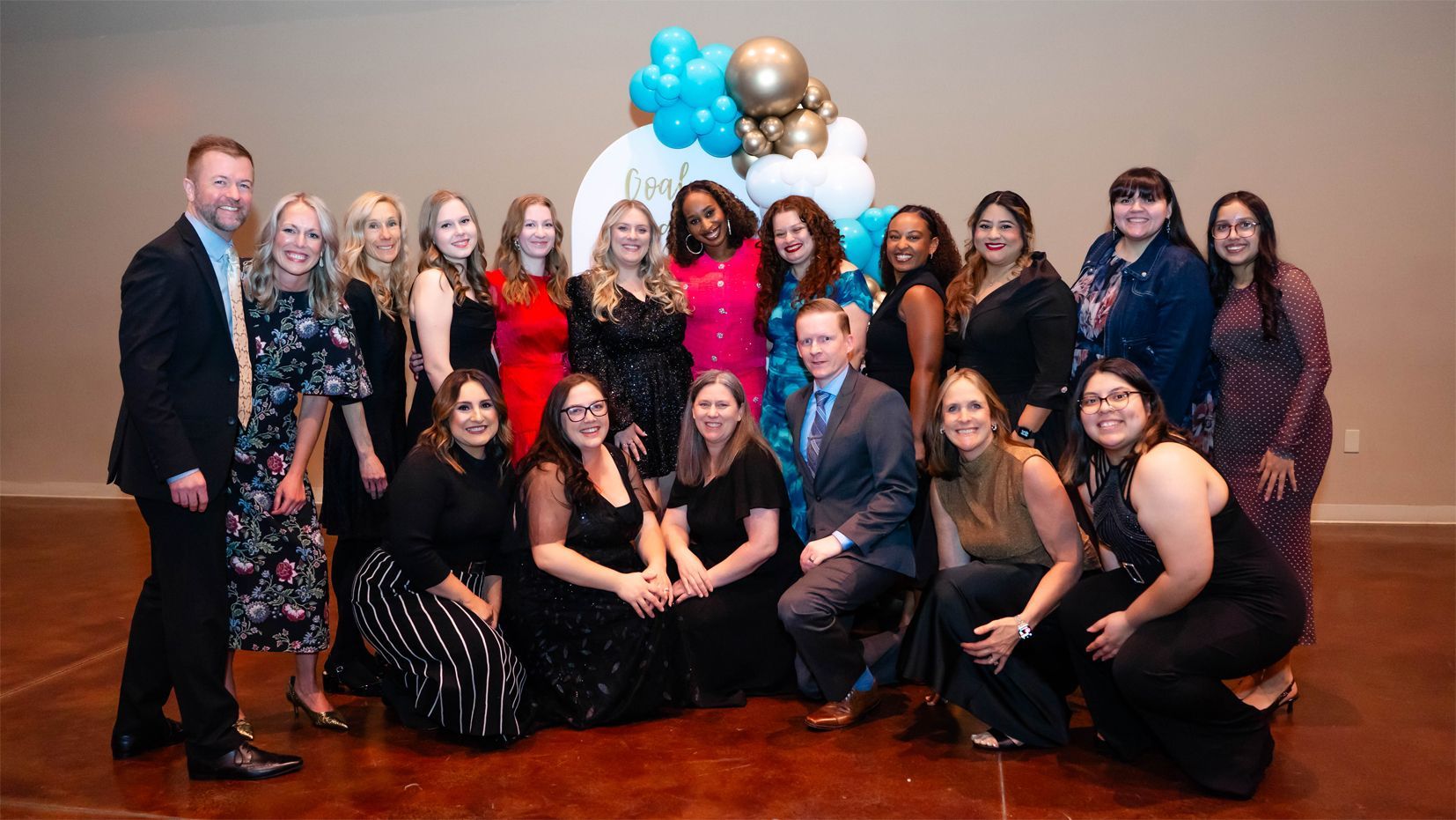 A group of people standing together and smiling in front of a blue and white balloon display at an event.