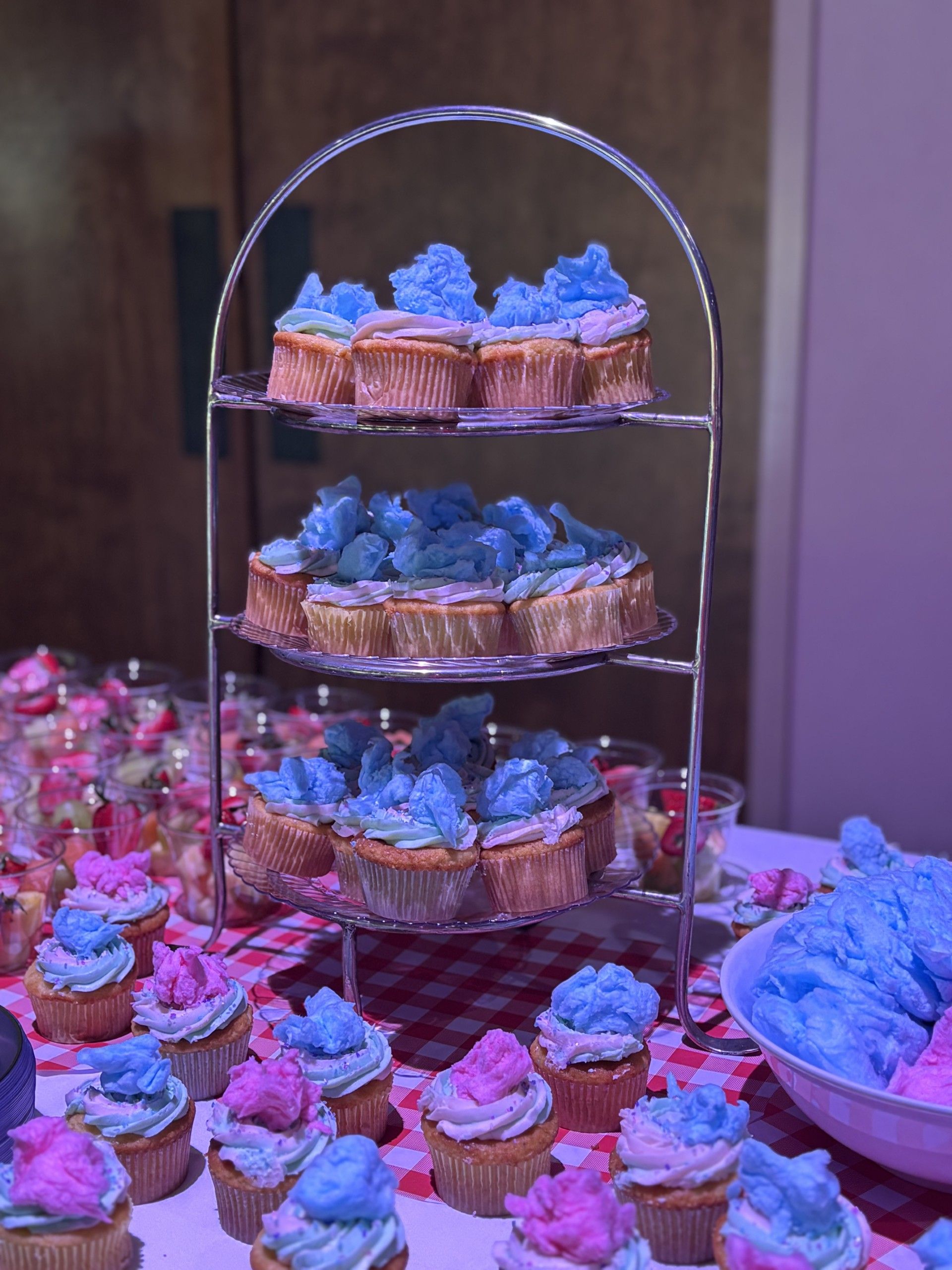 Three-tier dessert stand with blue-frosted cupcakes on a pink-lit table