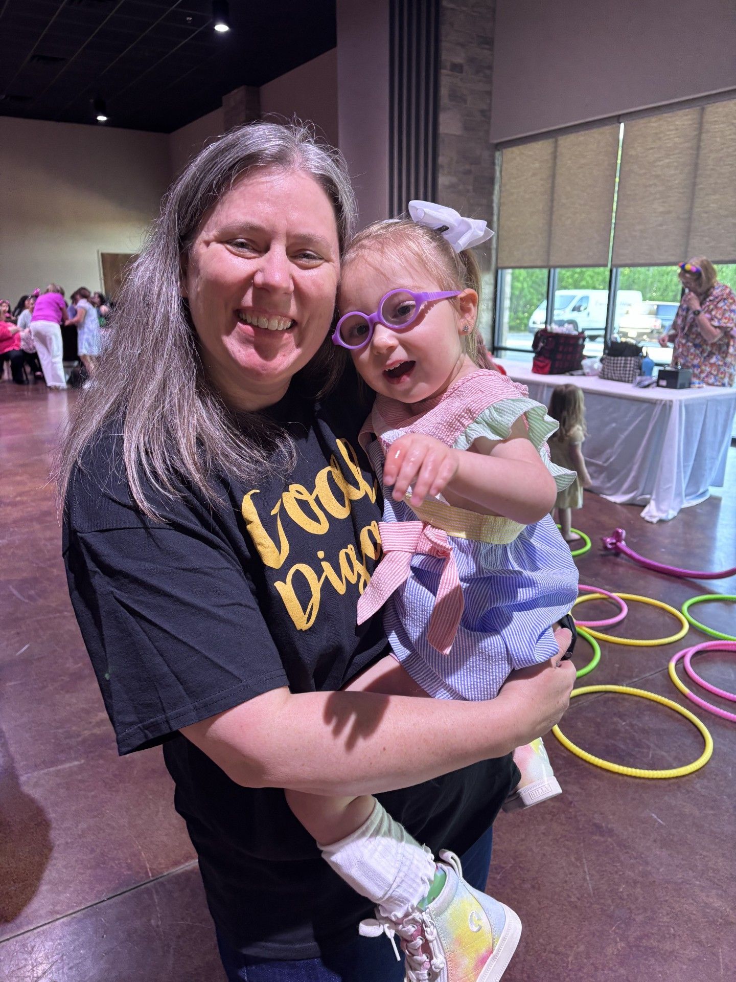 Smiling woman holding a child indoors near colorful floor hoops and tables