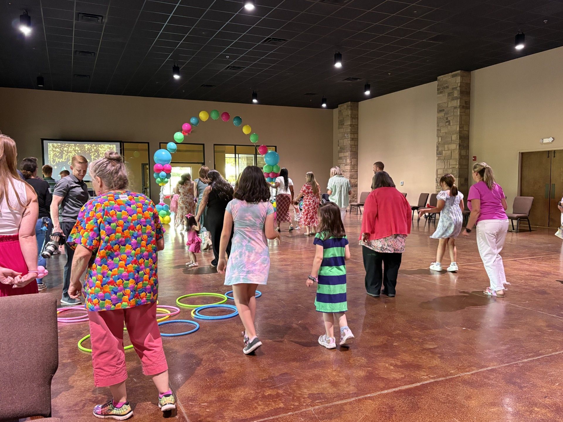People dancing in a decorated hall with colorful balloon arch and streamers.