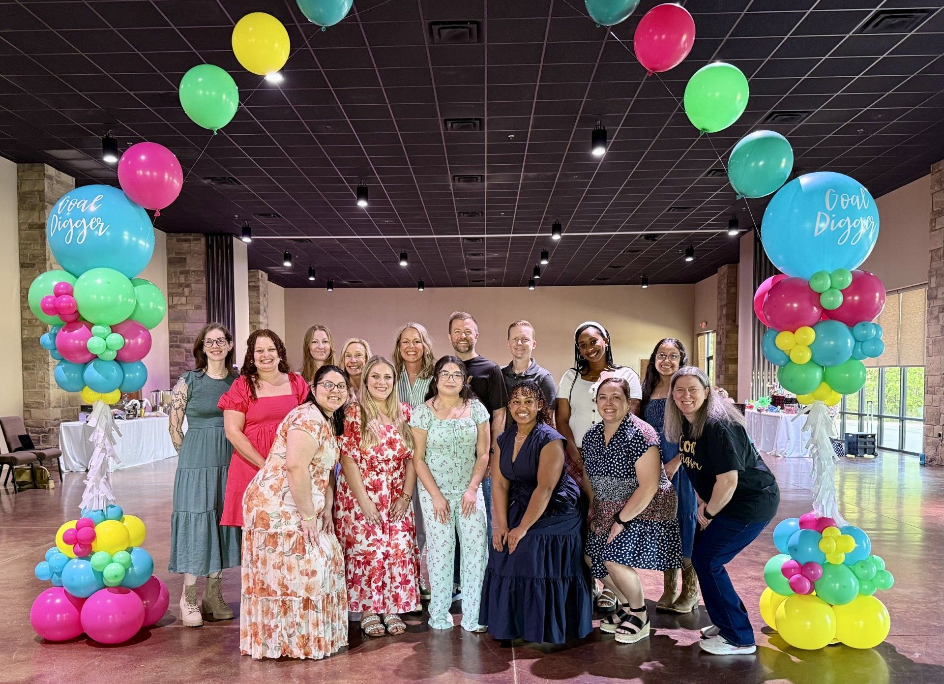 Group of people posing under colorful balloon arch in a decorated indoor event space