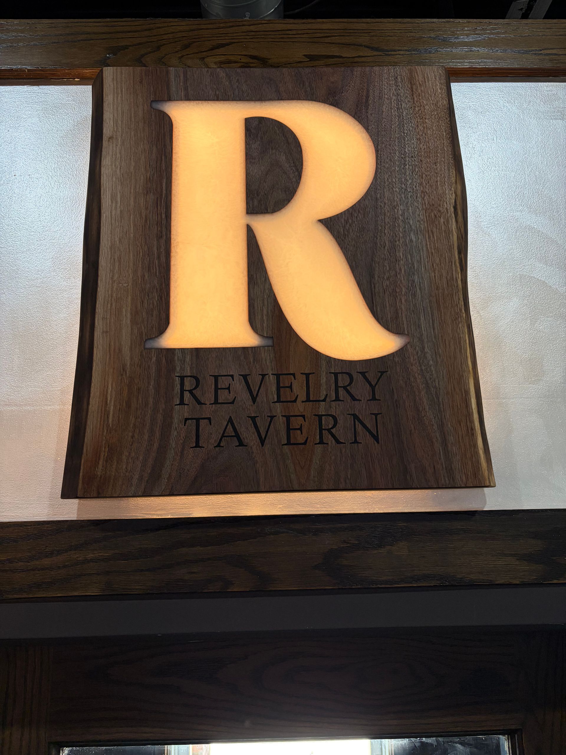 Illuminated R sign for Revelry Tavern on a dark wood plaque