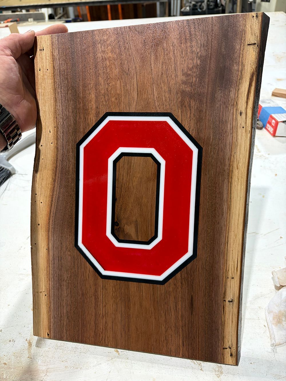 Red block letter “O” on a weathered wooden board being held in a workshop