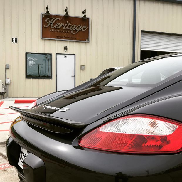Black sports car parked outside a Heritage building, rear view with red taillight.