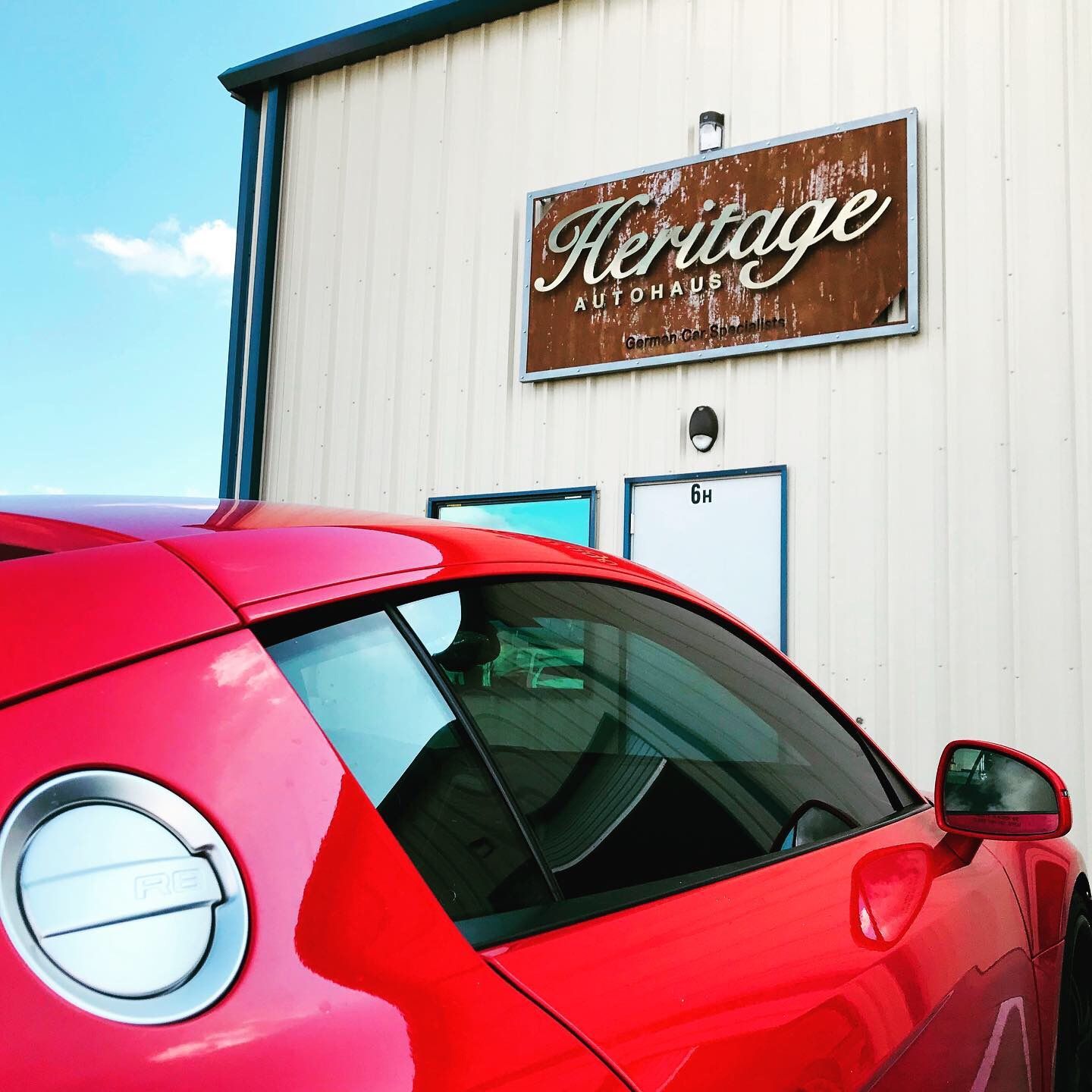 Red car parked beside a white building with a “Heritage” sign above the door