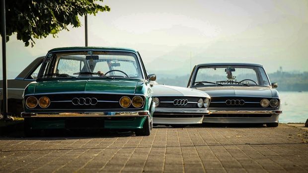 Three classic cars parked side by side on a paved road under trees, front view at sunset.