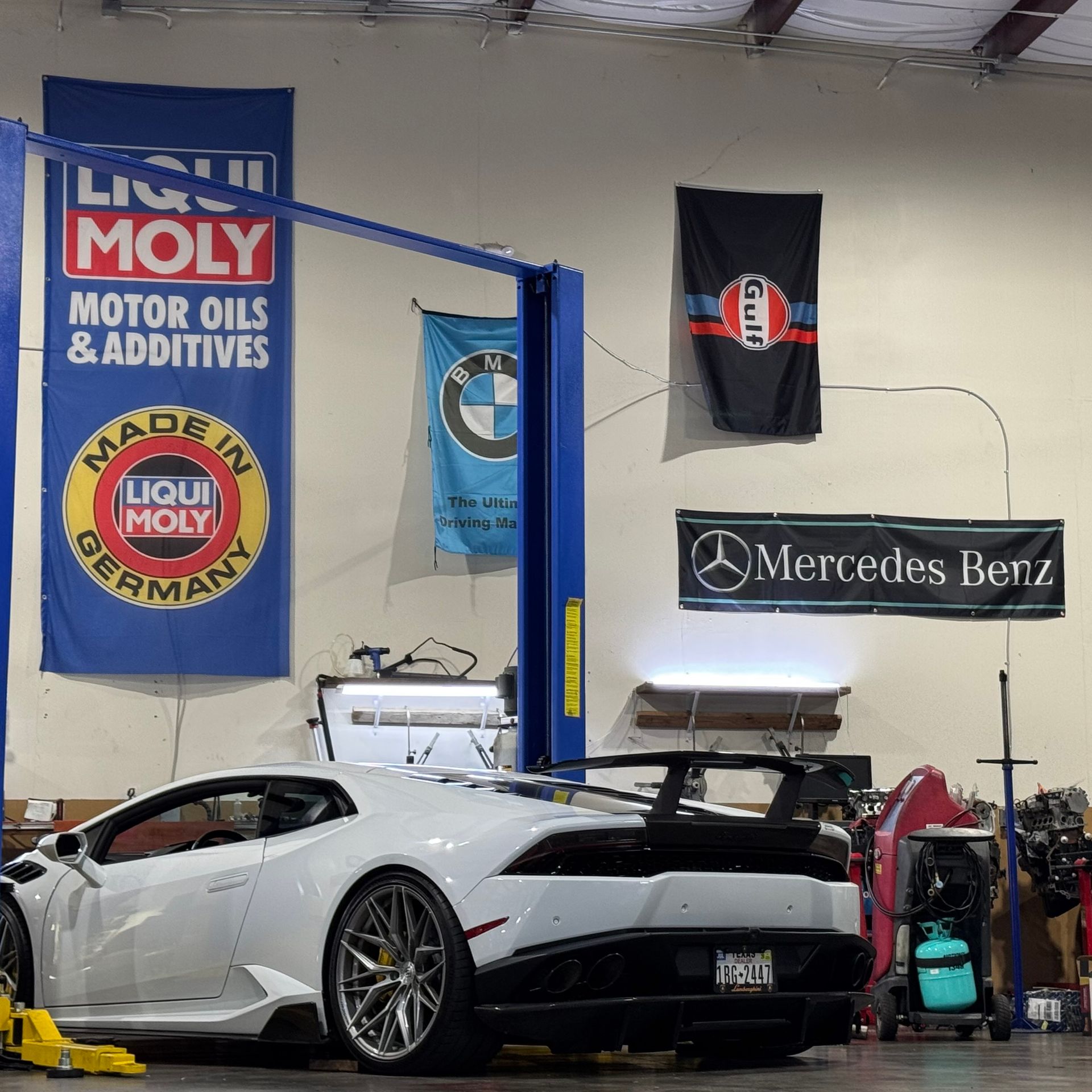 White sports car in an auto shop garage with BMW and Mercedes-Benz signs on the wall
