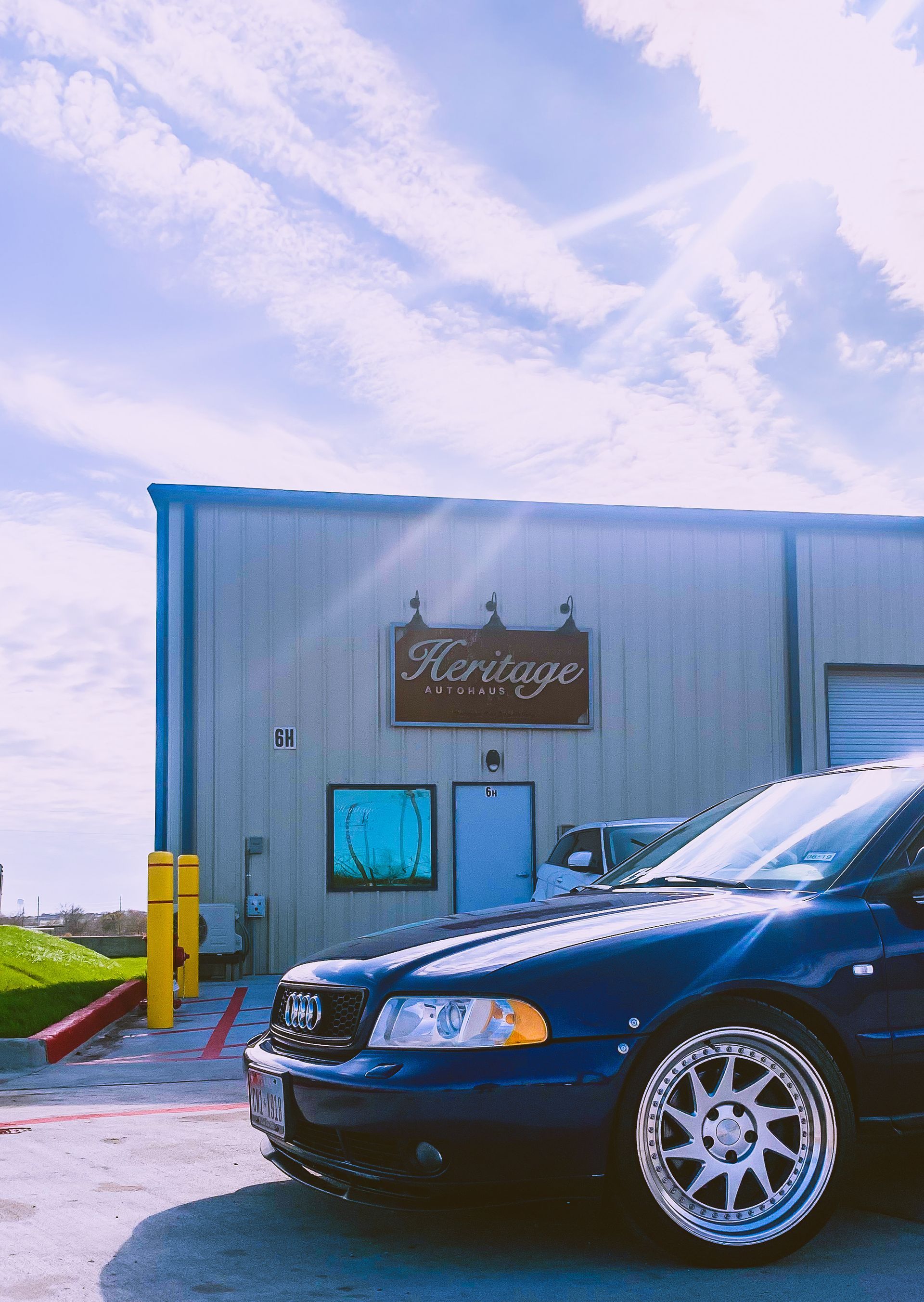 Black sedan parked beside a blue-and-white building under a cloudy sky
