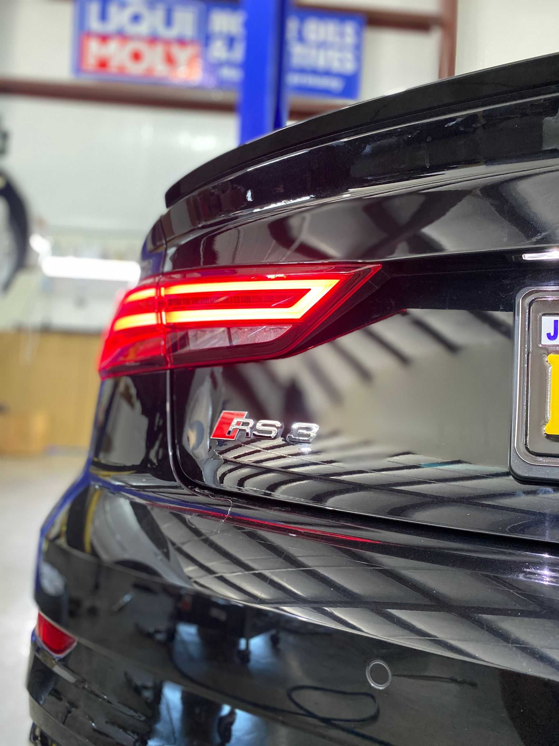 Rear view of a black Audi RS5 with illuminated taillights in a garage.