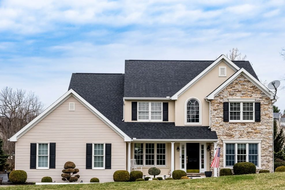 A large house with a black roof and white siding is sitting on top of a lush green hill.