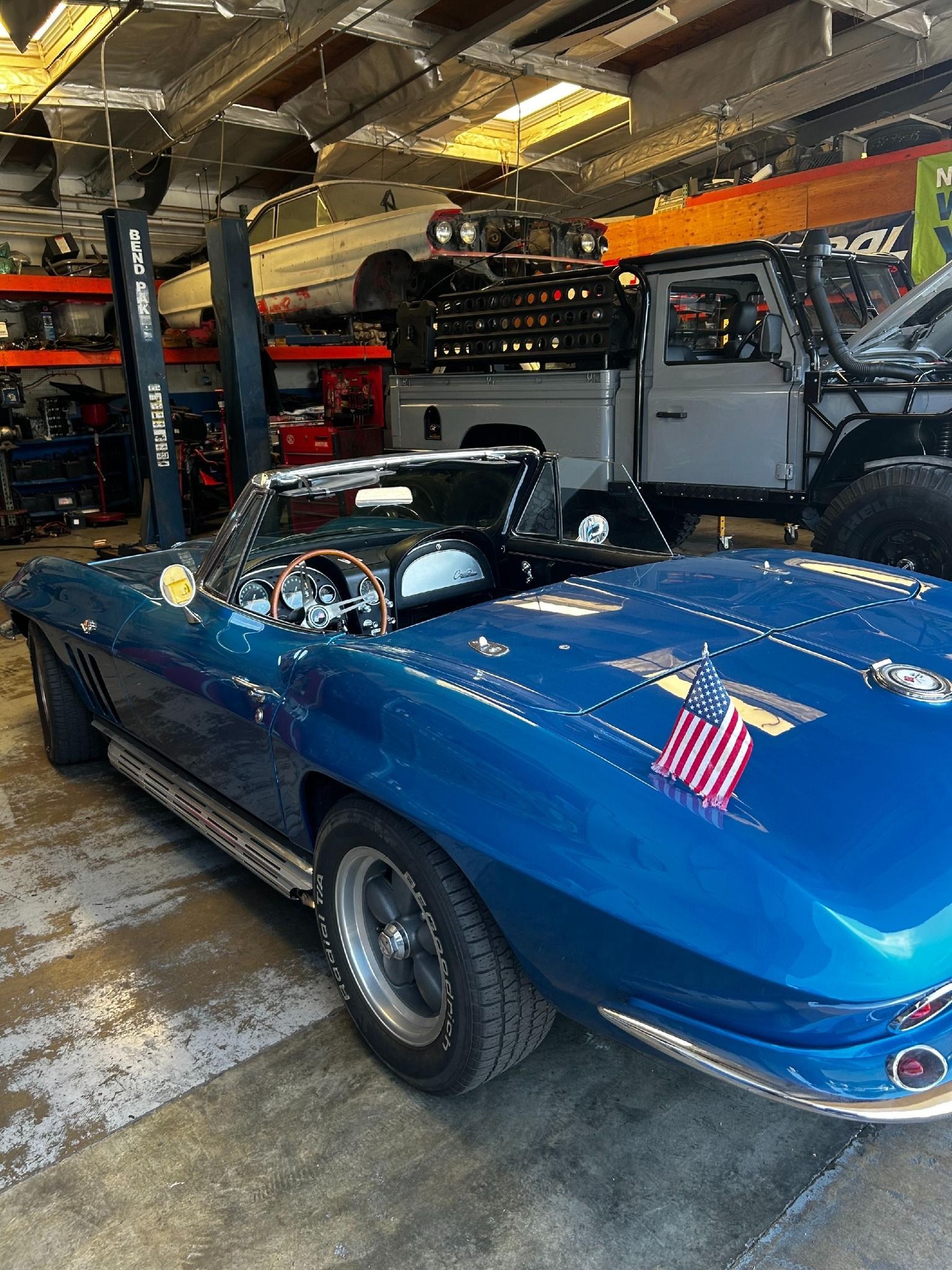 Blue classic convertible car in a garage with other vehicles and tools.