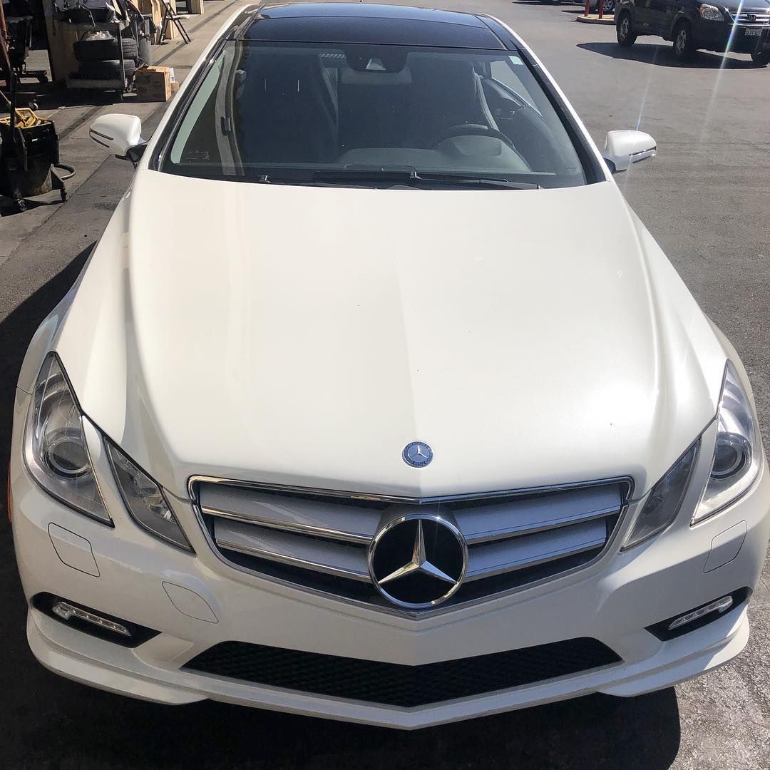 White Mercedes-Benz coupe parked on a city street, with a black roof and silver grill.