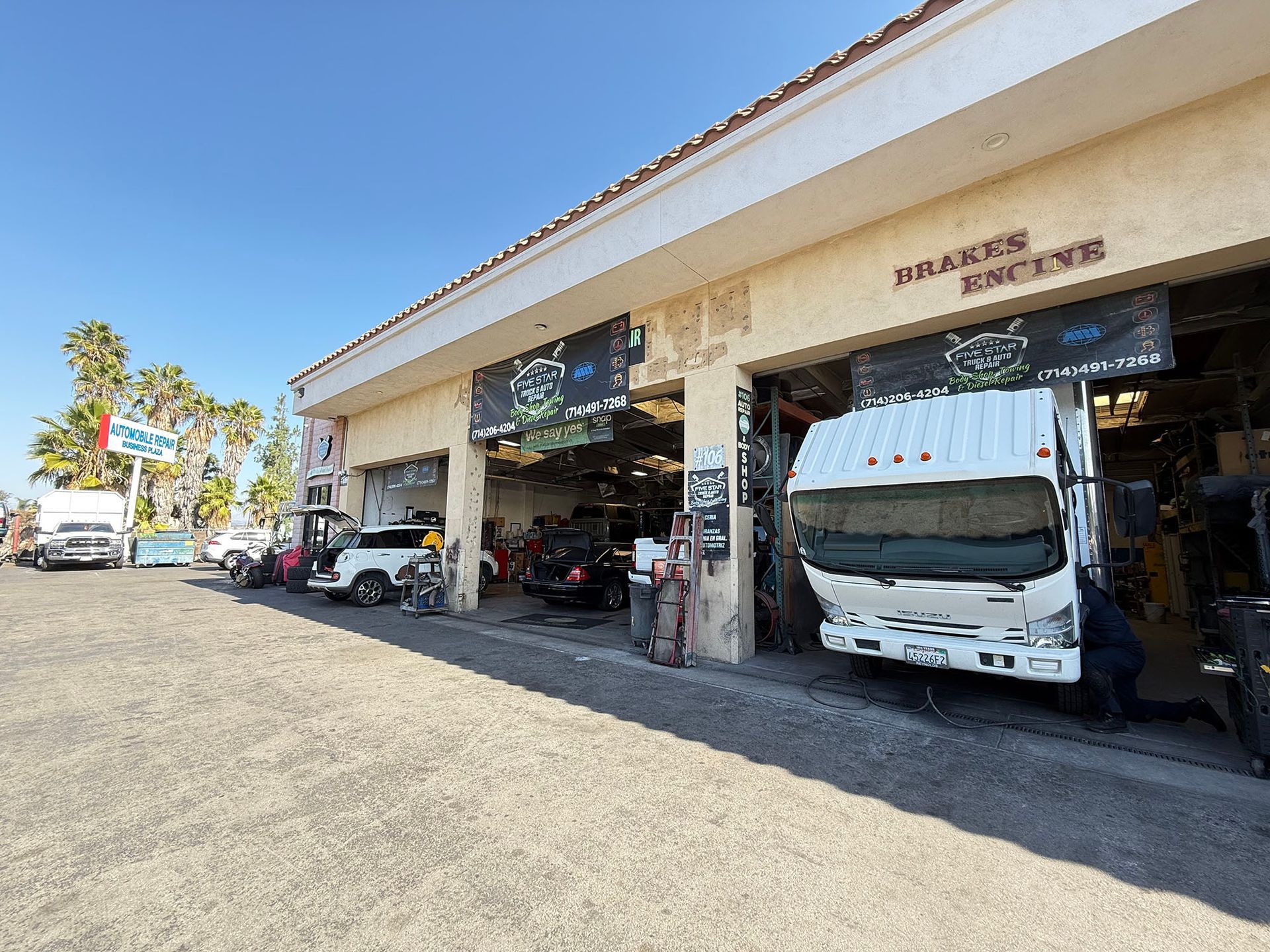 Auto repair shop exterior with a truck in a bay, sunny day.