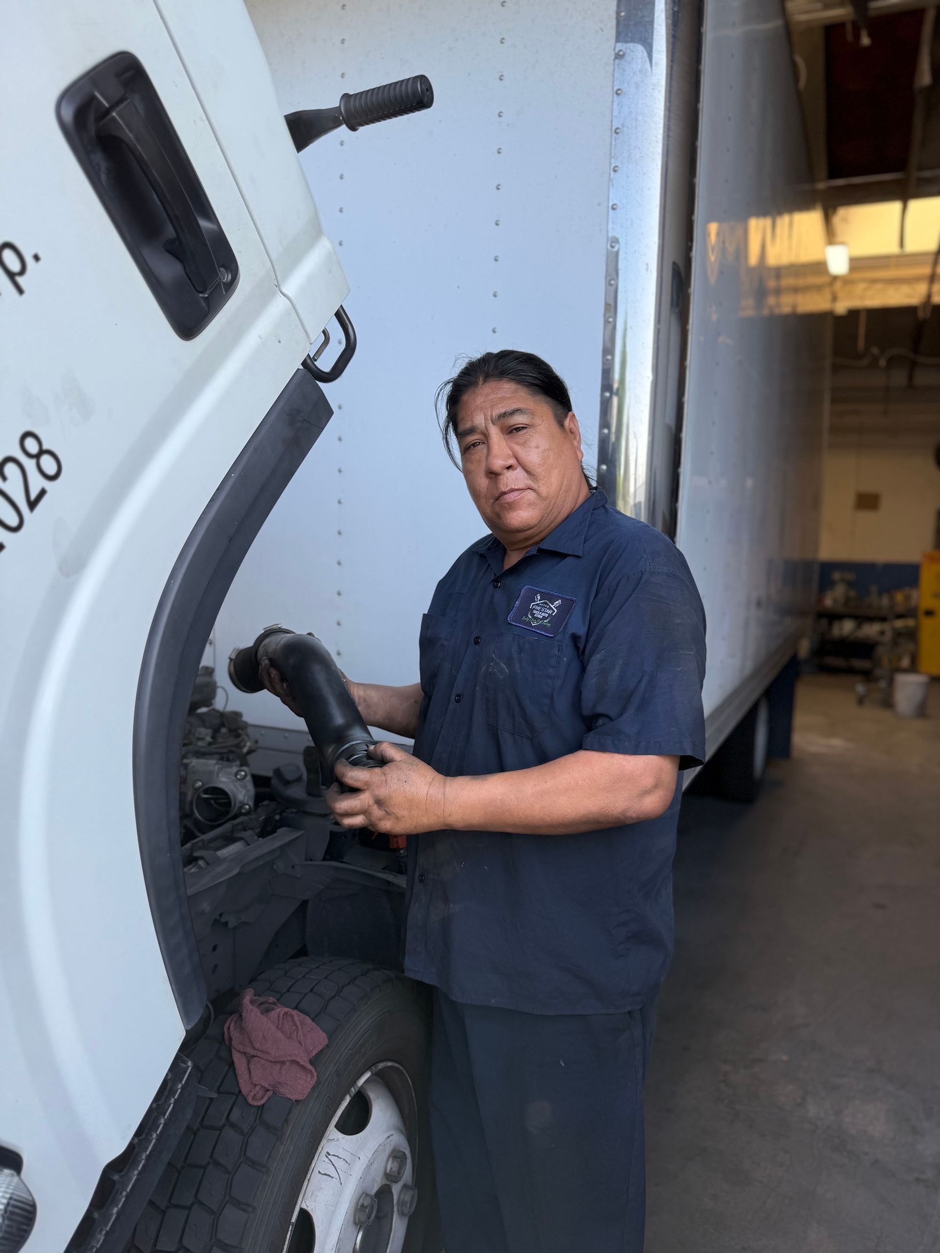 Mechanic working on a truck. Man in blue uniform inspecting engine. Truck parked inside a garage.