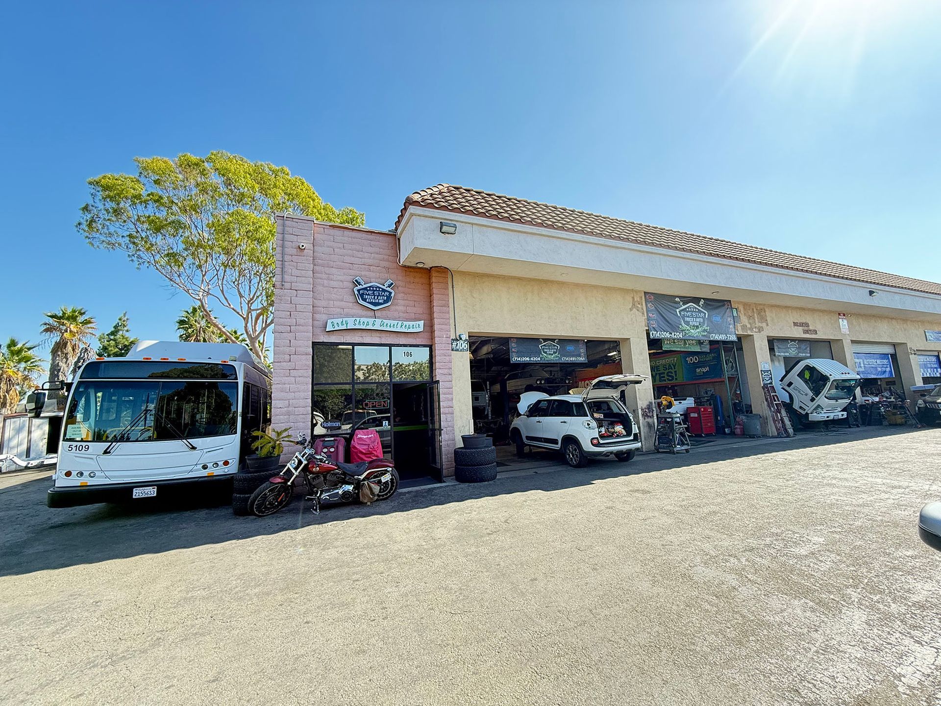 A sunny auto repair shop with a bus and vehicles being serviced in California.
