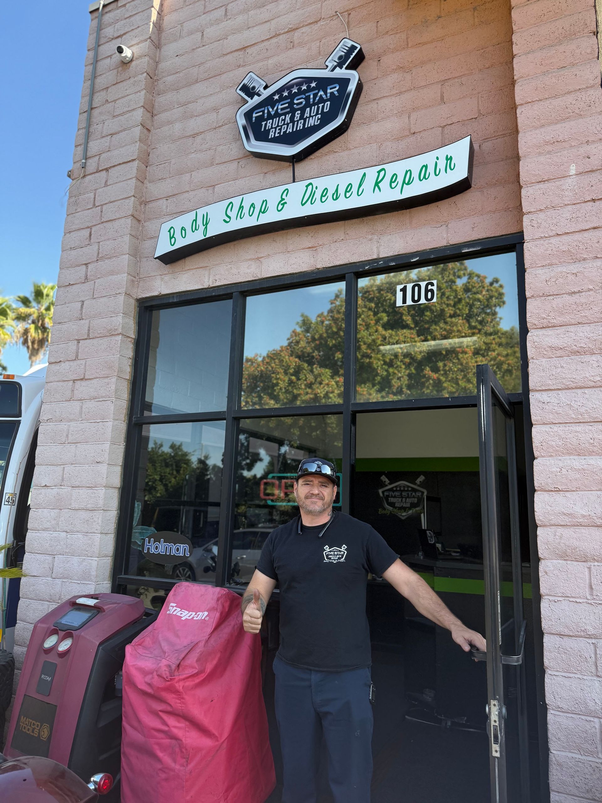 Man stands in doorway of Golf Carts & Vessel Repairs shop, giving a thumbs up. Shop has sign overhead.