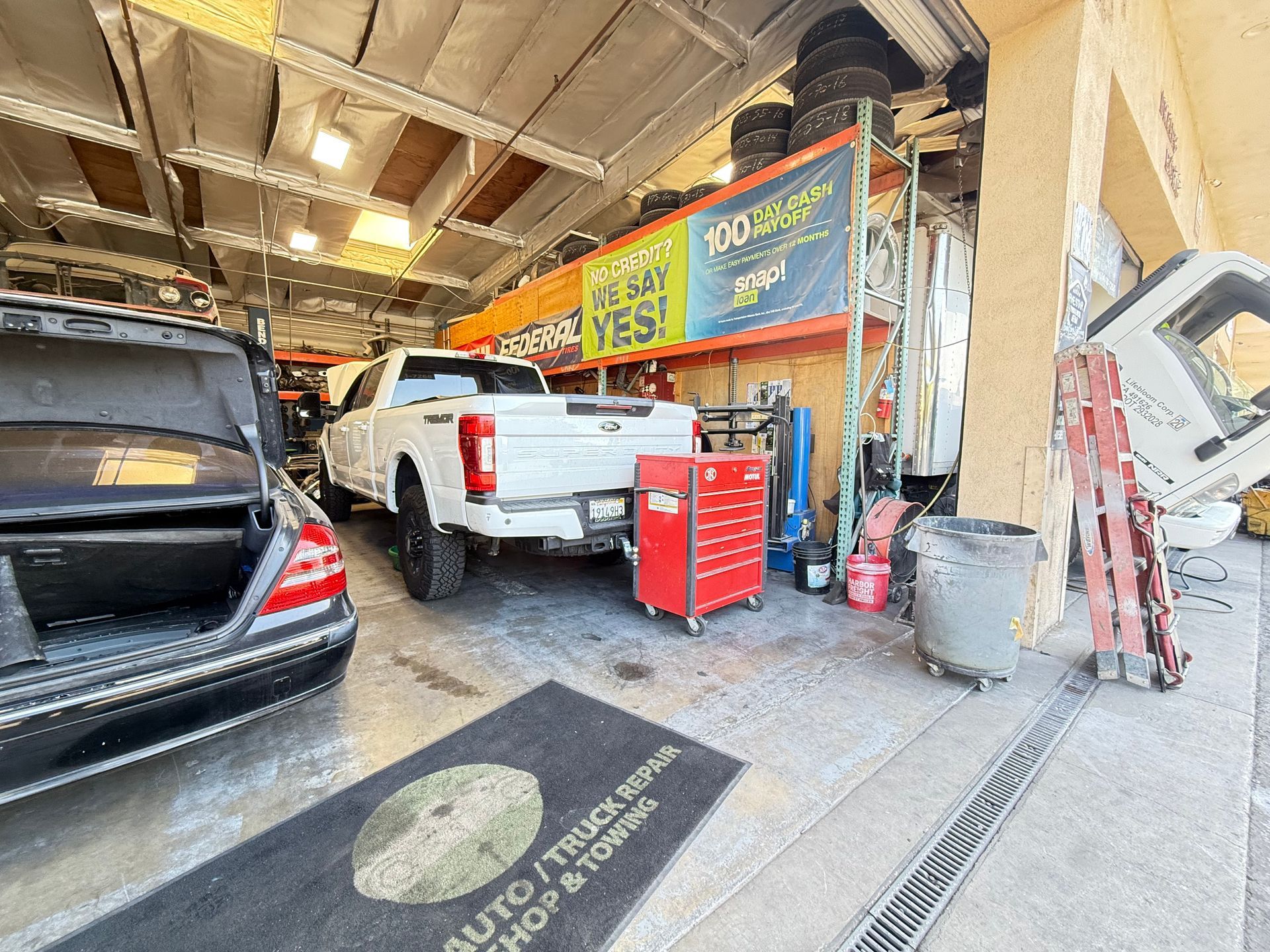 Auto repair shop: White pickup truck inside, black car, tools, tire storage, open bay.