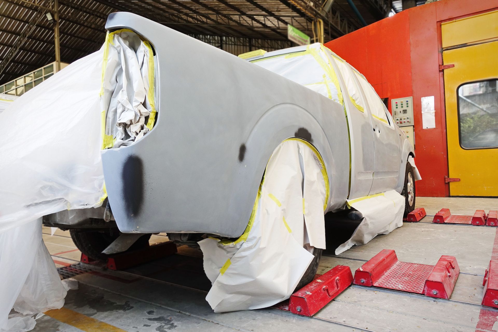 Car being prepped for painting in a body shop; covered in paper and tape.