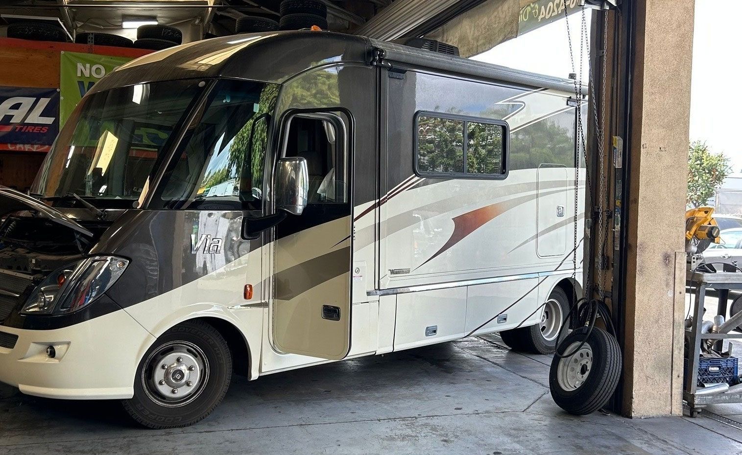 RV parked inside a garage. It has a cream and dark gray exterior with a side awning and open door.