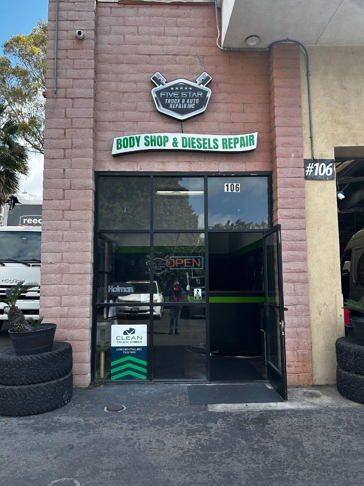 Body shop with green signage and open black door. Brick facade.