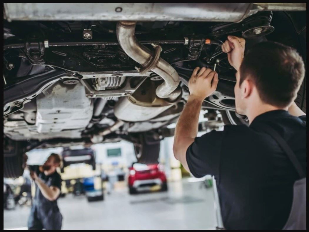 Mechanic working under a car in a garage, adjusting parts with tools.