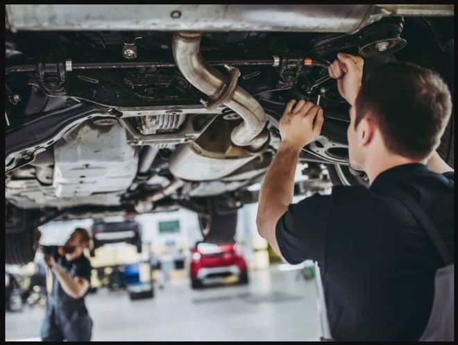 Mechanic working under a car in a garage, adjusting parts with tools.
