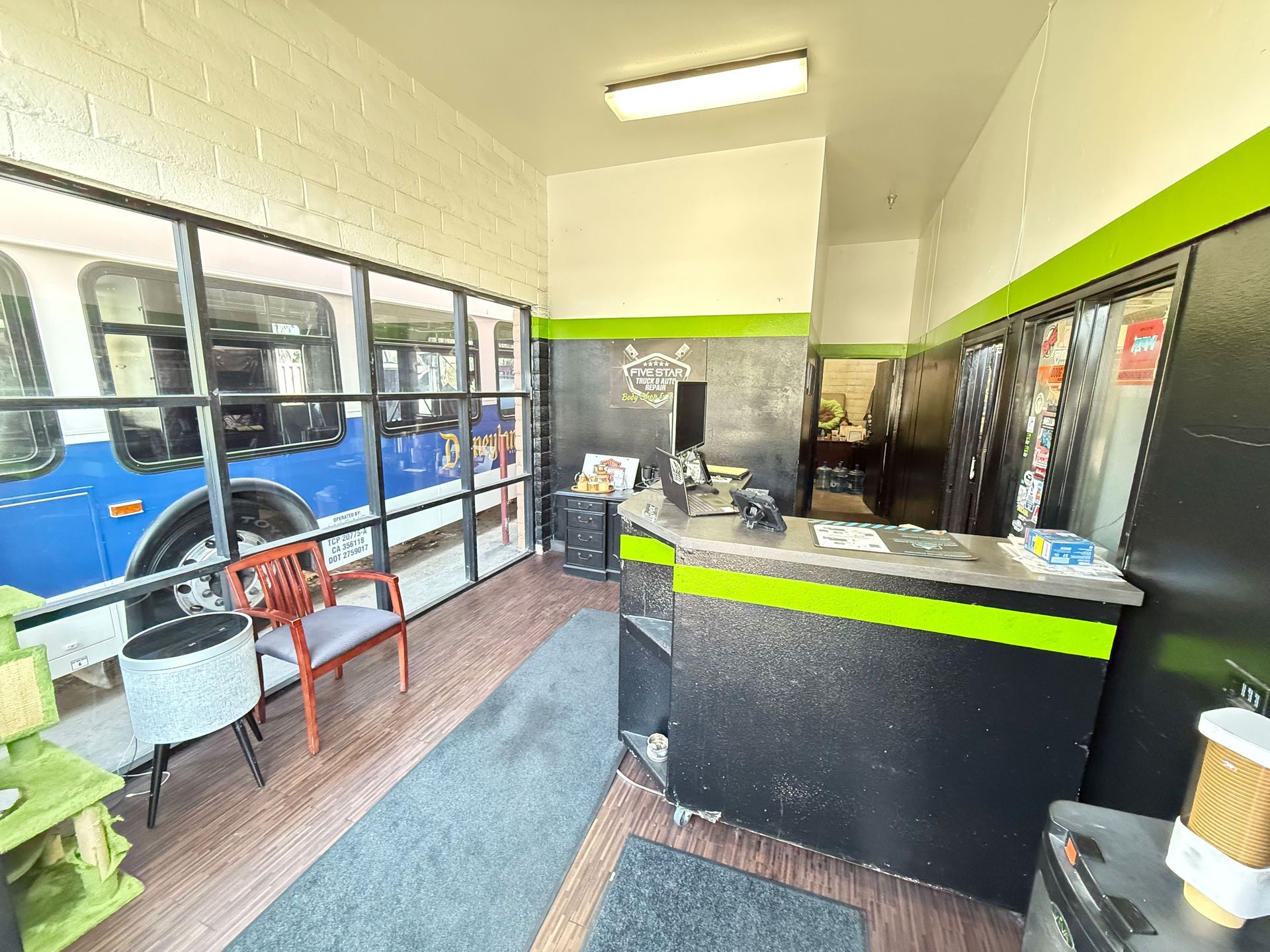 Interior of a shop with a bus partially visible through a window. Black and green desk and seating.