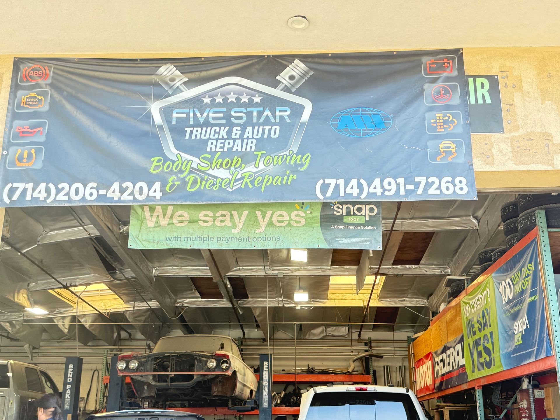 Banner for Five Star Truck & Auto Repair with phone numbers and cars on lifts inside the shop.
