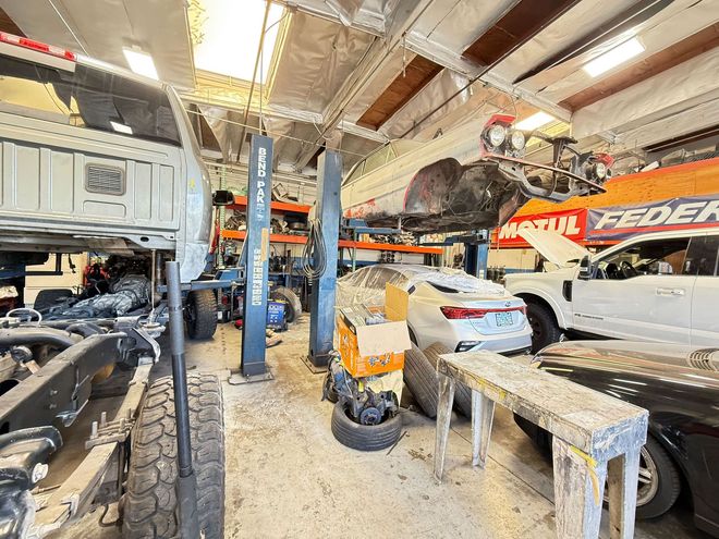 Interior of a car repair shop. Vehicles on lifts, parts scattered, cluttered, industrial setting.